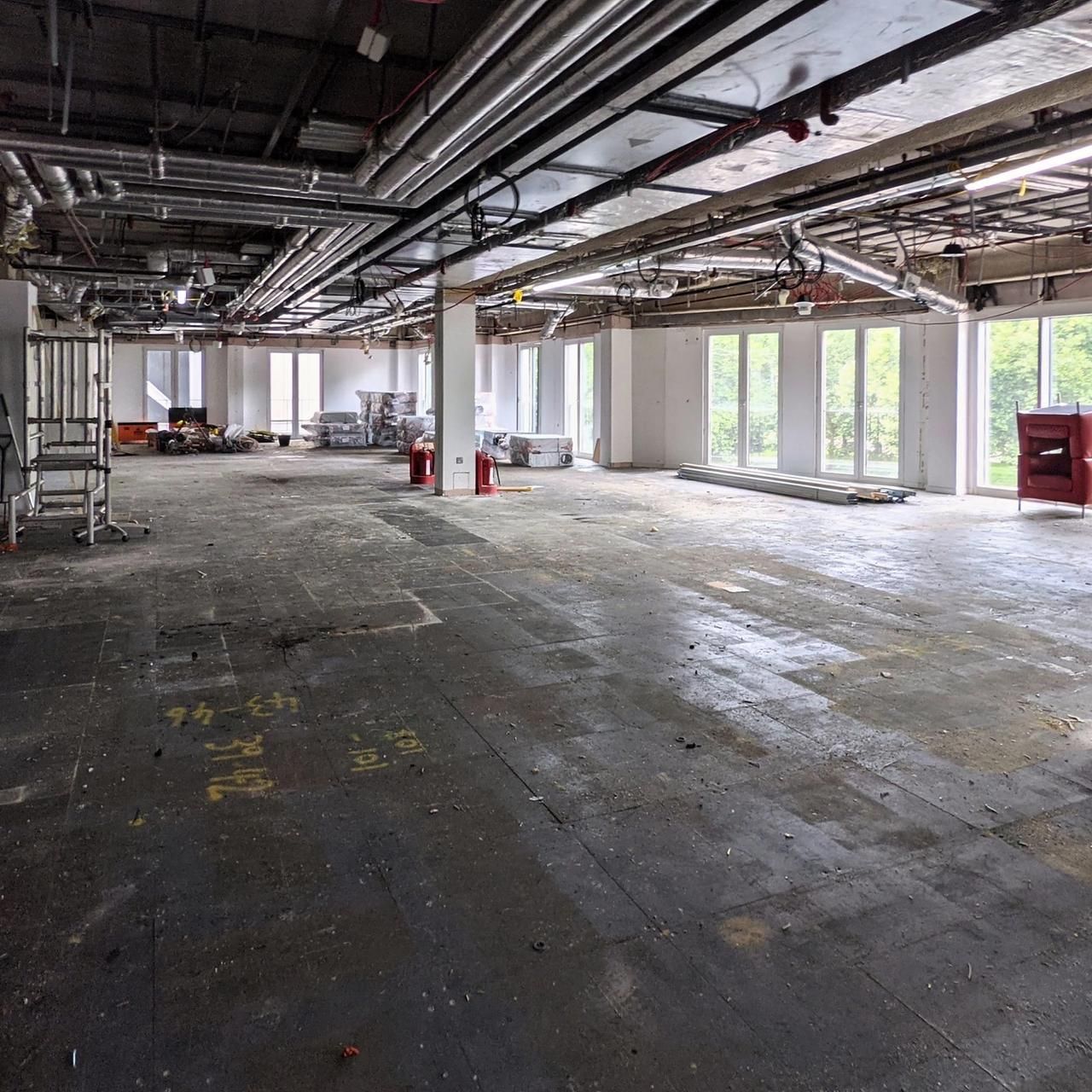 Stripped office floor in August 2021 with a column, exposed services and a ladder