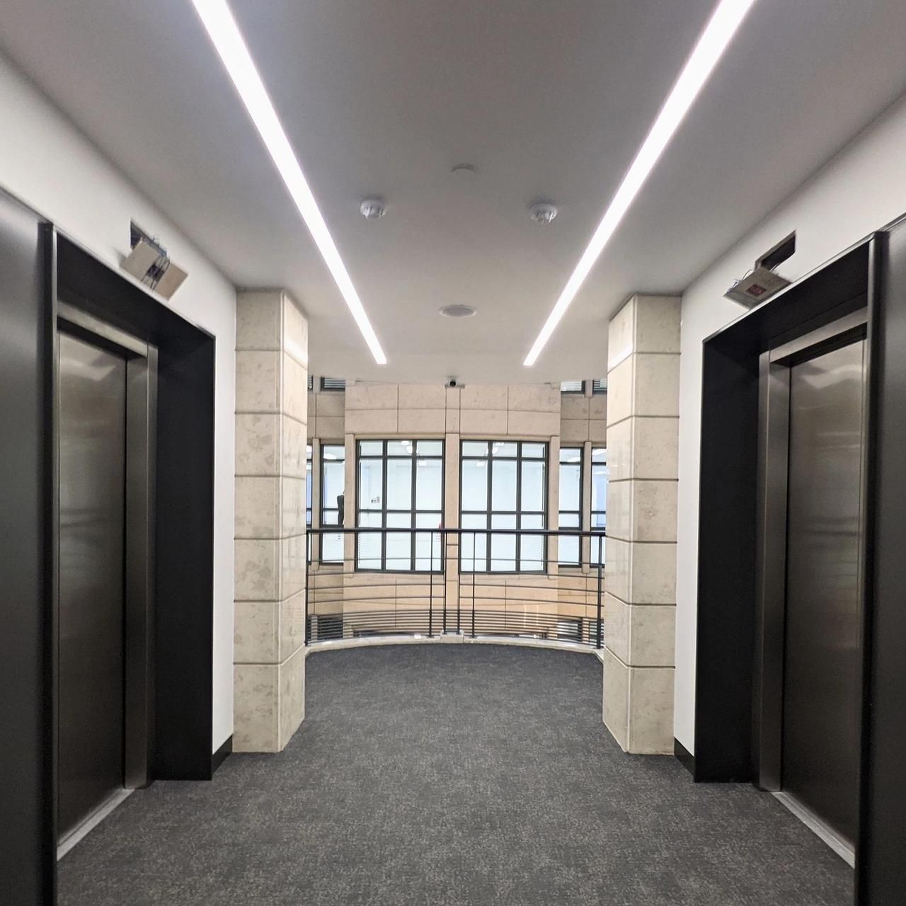 Lift lobby with dark lift doors, stone piers, a white ceiling with a lit cove and glazed doors beyond