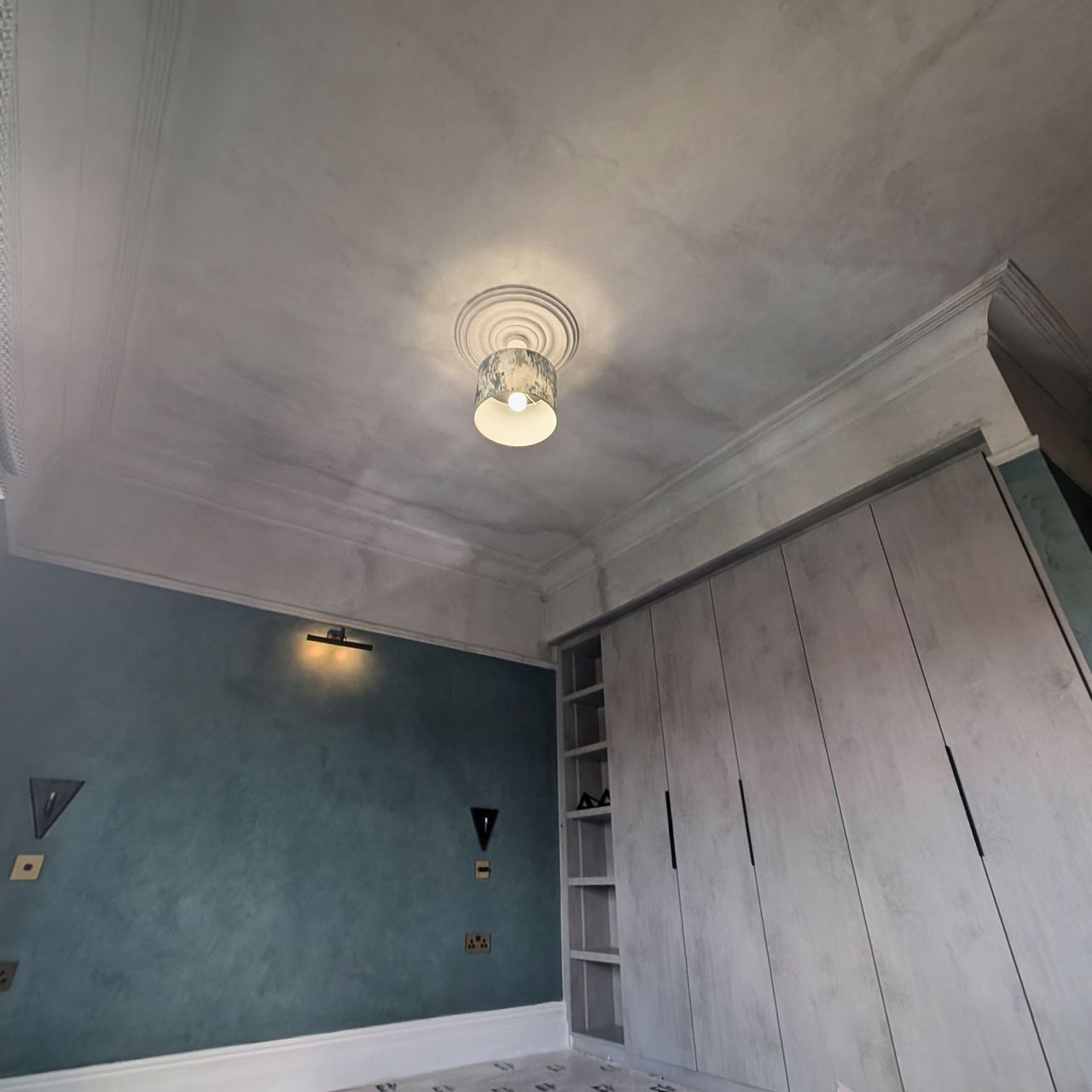 Fitted wardrobes scribed into a sloping eaves ceiling, beside a teal wall with a wall light and a ceiling light above