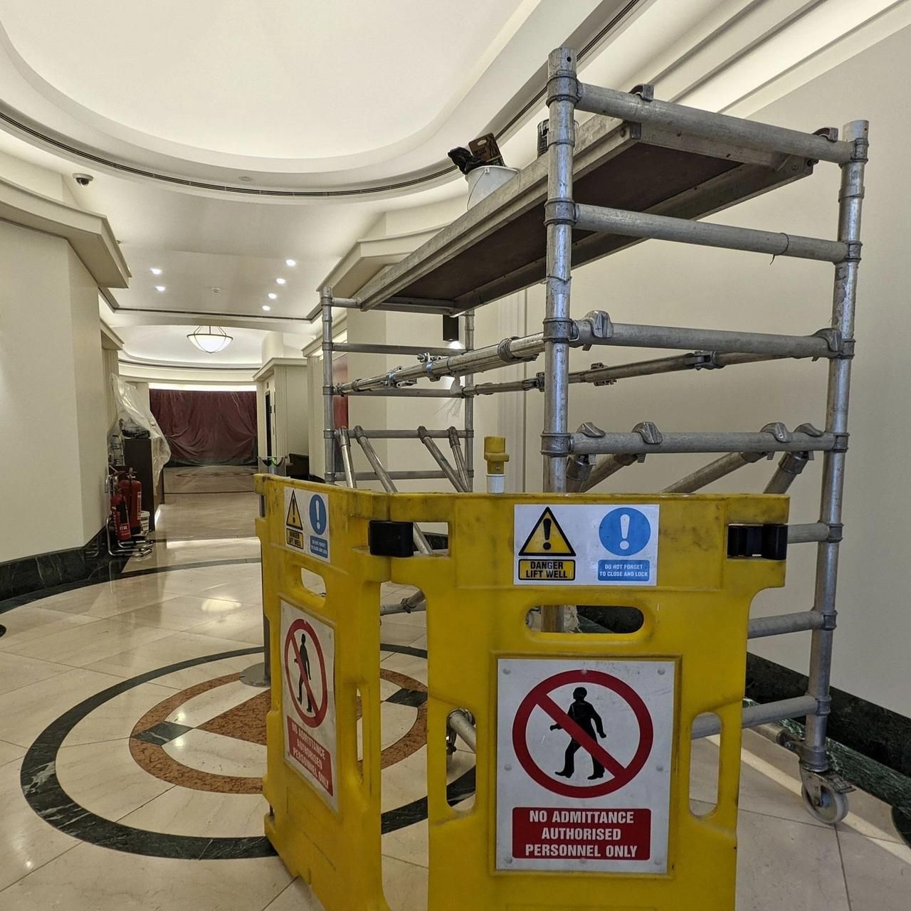 Scaffold tower on the terrazzo floor behind a yellow barrier, with the rest of the hall visible beyond