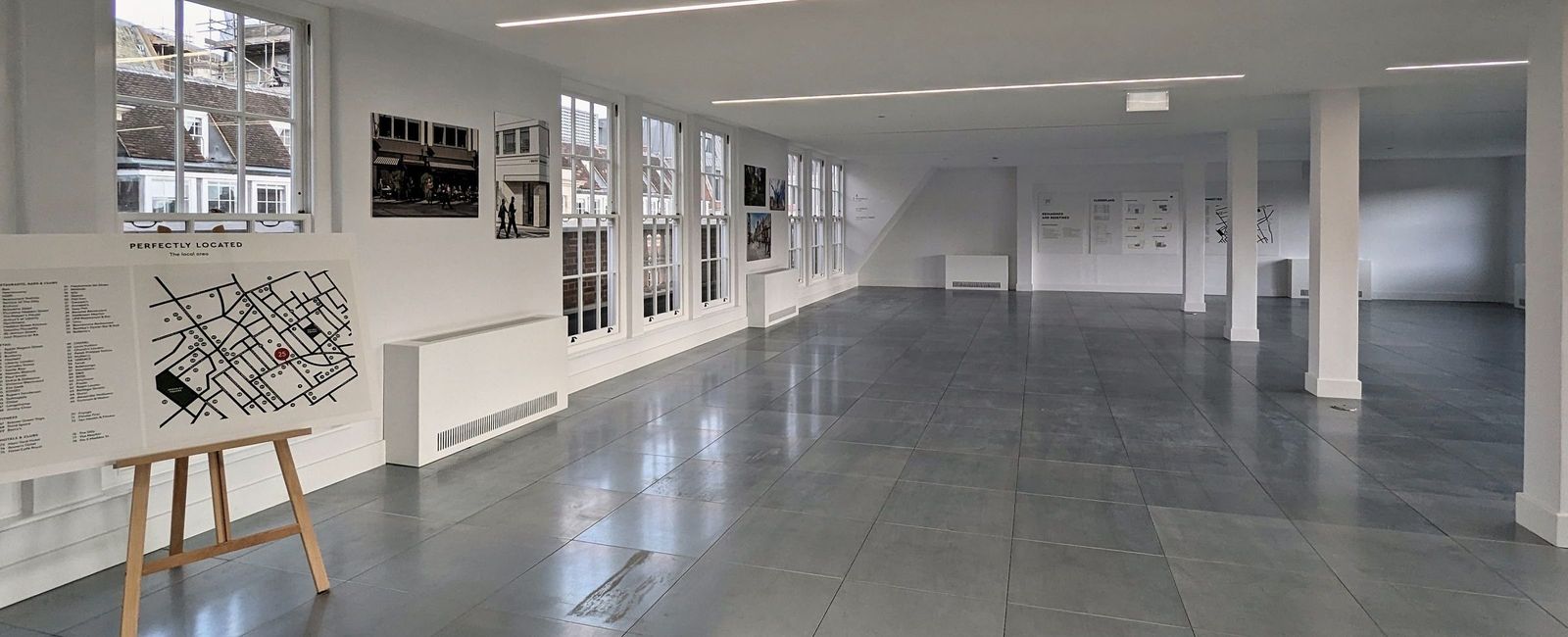 Finished office floor with grey polished floor, white columns, an easel with plans and sash windows, September 2023
