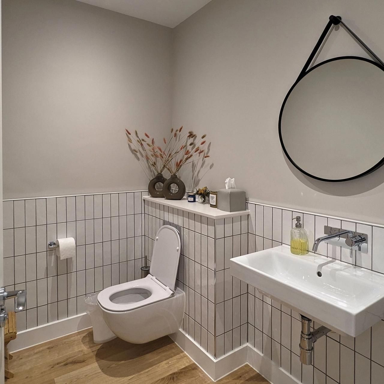 Cloakroom in one of the flats with white tiling, a round mirror and a timber floor