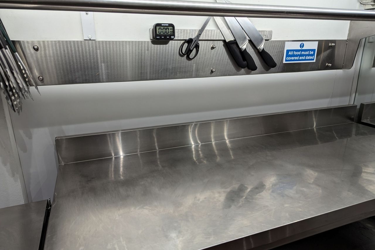 A full length stainless steel splashback above a stainless steel prep bench, with a magnetic knife rack