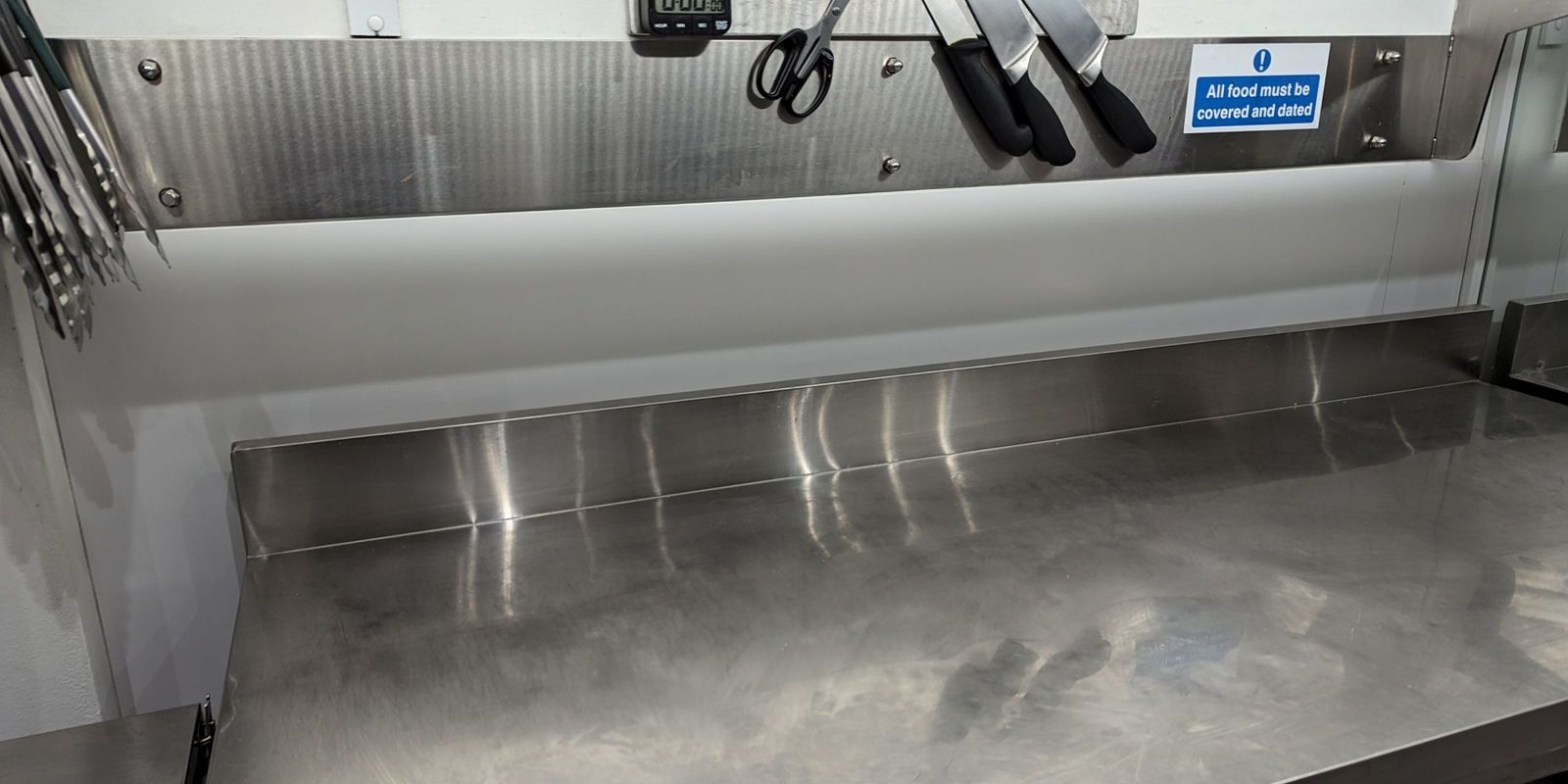 A full length stainless steel splashback above a stainless steel prep bench, with a magnetic knife rack